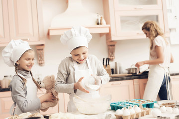 Children with mother in kitchen. Brother and sister are adding flour to dough.