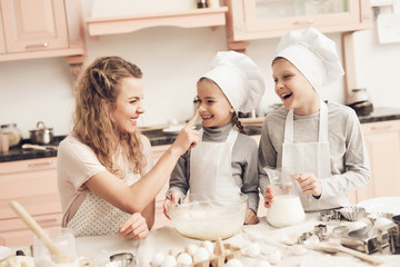 Children with mother in kitchen. Family is playfully smearing dough on nose.