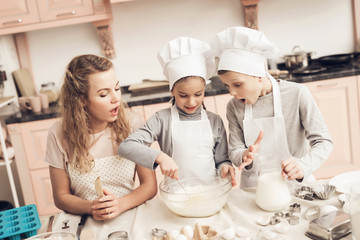 Children with mother in kitchen. Sister is stirring dough and brother is holding milk.