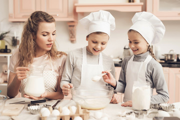 Children with mother in kitchen. Kids are adding flour and mother is adding milk in bowl.
