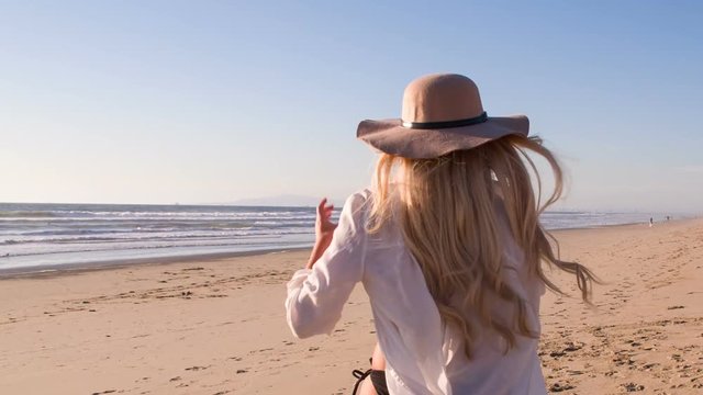 Attractive blond woman walking on the beach at sunset. Slow Motion.