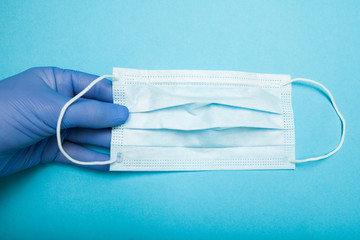 The doctor's hand in a blue medical glove holds a sterile mask.