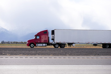 Red big rig semi truck carry refrigeration semi trailer and going by flat road in Utah