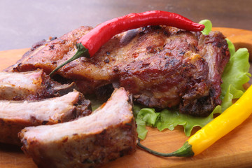 grilled barbecued ribs with lettuce leaves, hot chili pepper and sauce on wooden cutting board.