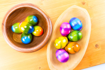 Colored by hand Easter eggs in a natural oak and ipe wood bowls isolated on a wood counter top board over view
