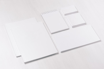 White blank business card, envelope, brochure, notepad, stickers on soft white wood board, inclined.