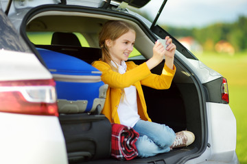 Adorable little girl ready to go on vacations with her parents. Kid playing with her phone in a car.
