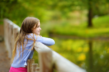 Cute little girl watching animals at the zoo on warm and sunny summer day. Child watching zoo animals. © MNStudio