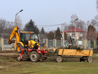 Debowiec/Poland - March 27, 2018: Spring cleaning of green territory in the city. Tractor and excavator for upgrading the green plantations of streets. The work of the municipal public utility.