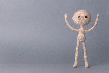 A toy man on a gray background with space for text. Knitted toy amigurumi. Presentation. Motivational phrase. Cute model. Puppet. Sweet doll. Hand up