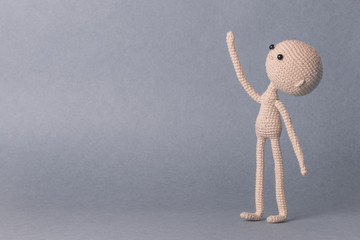 A toy man on a gray background with space for text. Knitted toy amigurumi. Presentation. Motivational phrase. Cute model. Puppet. Sweet doll. Hand up. Looks up.