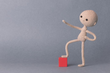 A toy man on a gray background with space for text. Knitted toy amigurumi. Presentation. Motivational phrase. Cute model. Puppet. Sweet doll. Hand up. achieving the goal.