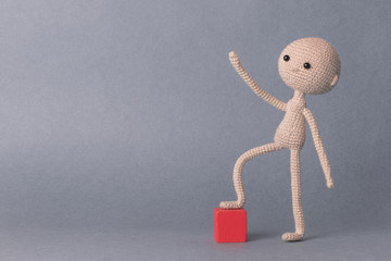A toy man on a gray background with space for text. Knitted toy amigurumi. Presentation. Motivational phrase. Cute model. Puppet. Sweet doll. Hand up. achieving the goal.