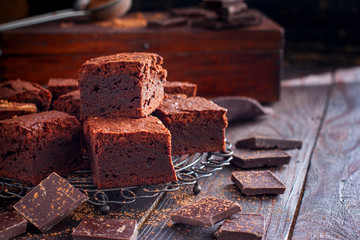 Homemade brownies of dark chocolate on a metal stand with chocolate slices on a wooden table, horizontal, copy space
