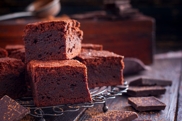 Homemade brownies of dark chocolate on a metal stand with chocolate slices on a wooden table, horizontal, copy space