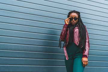 Naklejka premium portrait of beautiful stylish young african american woman adjusting sunglasses and looking at camera