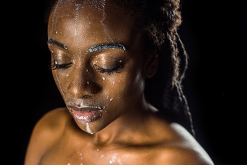 beautiful sensual young african american woman with spilled milk on face isolated on black