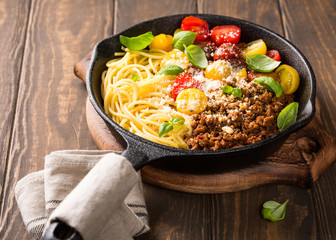 Healthy italian food. Delicious spaghetti Bolognaise or Bolognese with savory minced beef and cherry tomatoes garnished with parmesan cheese and basil in cost iron pan. Copy space.