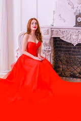 Magnificent young woman in luxurious red dress and precious jewelery posing in a luxury apartment. Classic vintage interior. Beauty luxury fashion 