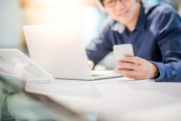 Young Asian business man using smartphone while working with laptop computer in co working space. freelance or digital nomad lifestyle concepts