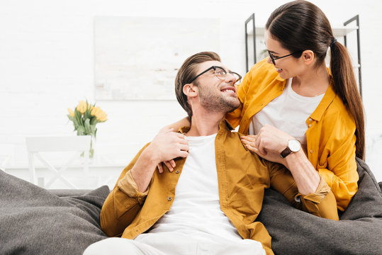 Woman Embracing Her Boyfriend From Behind While He Sitting On Couch At Home