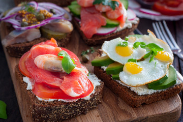 An open sandwich with red fish, shrimps, fresh vegetables on rye bread with curd cheese, selective focus