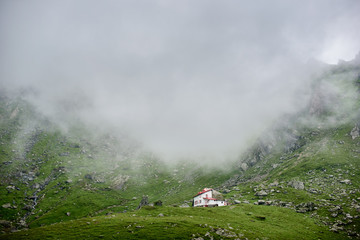 Low angle shot of a small white cozy house on the hill in the foggy mountains copyspace living lifestyle wilderness nature environment friendly Europe traditional exploring tourism.