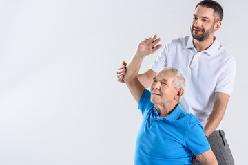 portrait of rehabilitation therapist helping senior man stretching isolated on grey