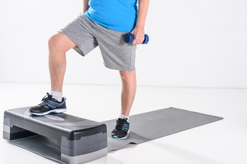 partial view of senior man with dumbbells exercising on stepper isolated on grey