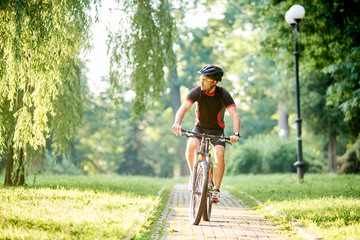 Toned man bicyclist looking to side while riding bicycle down park alley on summer day. Sportsman training thinking about future win in contest. Exercising, reaching goal