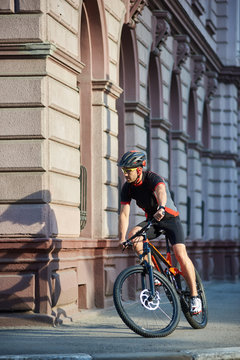 Sportsman in professional cycling clothes and protective helmet riding along old historical city streets, taking turns, performing tricks in urban area. Concept of healthy lifestyle