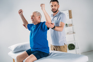 Obraz premium portrait of focused physiotherapist doing massage to senior man on massage table