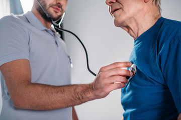 cropped shot of rehabilitation therapist with stethoscope checking senior mans heartbeat