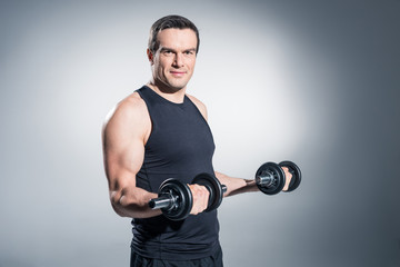 Fototapeta na wymiar Active man training with dumbbells on grey background