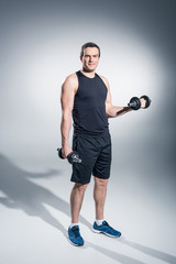 Fototapeta na wymiar Young man athlete exercising with dumbbells on grey background