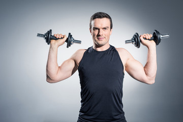Fototapeta na wymiar Confident sportive man exercising with dumbbells on grey background
