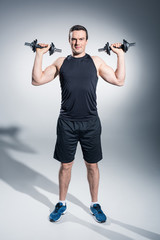 Fototapeta na wymiar Attractive man athlete lifting dumbbells on grey background