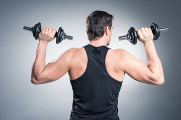 Fototapeta na wymiar Rear view of man exercising with dumbbells on grey background