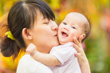 At the evening time before the sunset, 4 months baby feeling happy and smiles with her mother in the garden.