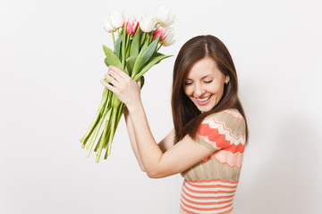 Naklejka premium Beautiful happy young brunette woman in light patterned dress is holding bouquet of white and pink tulips in hands, rejoices and looks down isolated on white background. Concept of holiday, good mood.