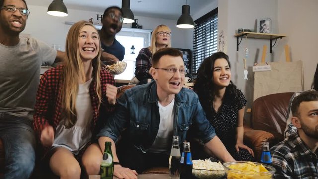 Diverse football fans get wild celebrating win 4K slow motion. Happy multi ethnic friends watching sports on TV. Emotion