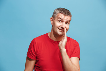 The young man whispering a secret behind her hand over blue background