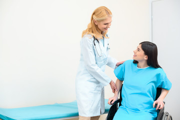 mature obstetrician gynecologist helping pregnant woman to sit down on wheelchair