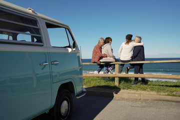 Senior friends on a road trip looking at the ocean, sit on fence