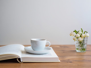 Weiße Tasse und Untertasse auf einem offenen Buch. Blumen.