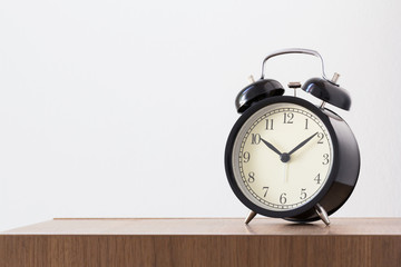retro black alarm clock on wooden table near white concrete wall