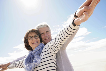 Portrait of senior couple at the beach stretching arms out