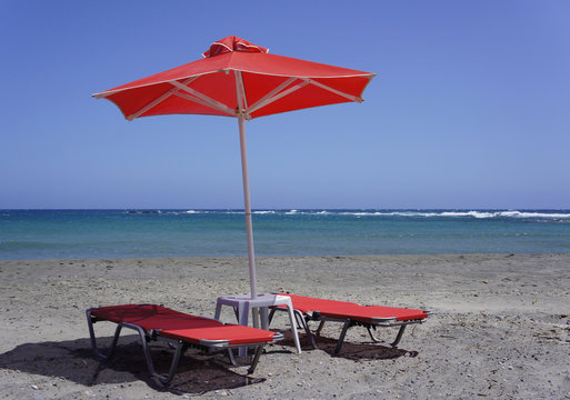 Red sun loungers and a red parasol on the sandy beach, natural beach
