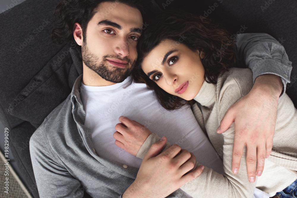 Wall mural high angle view of young couple hugging and looking at camera at home