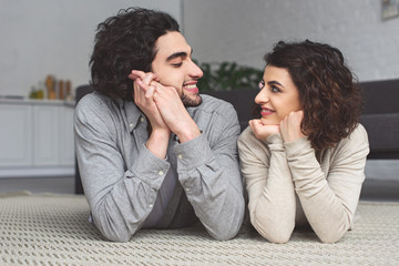 smiling young couple lying on floor and looking at each other at home